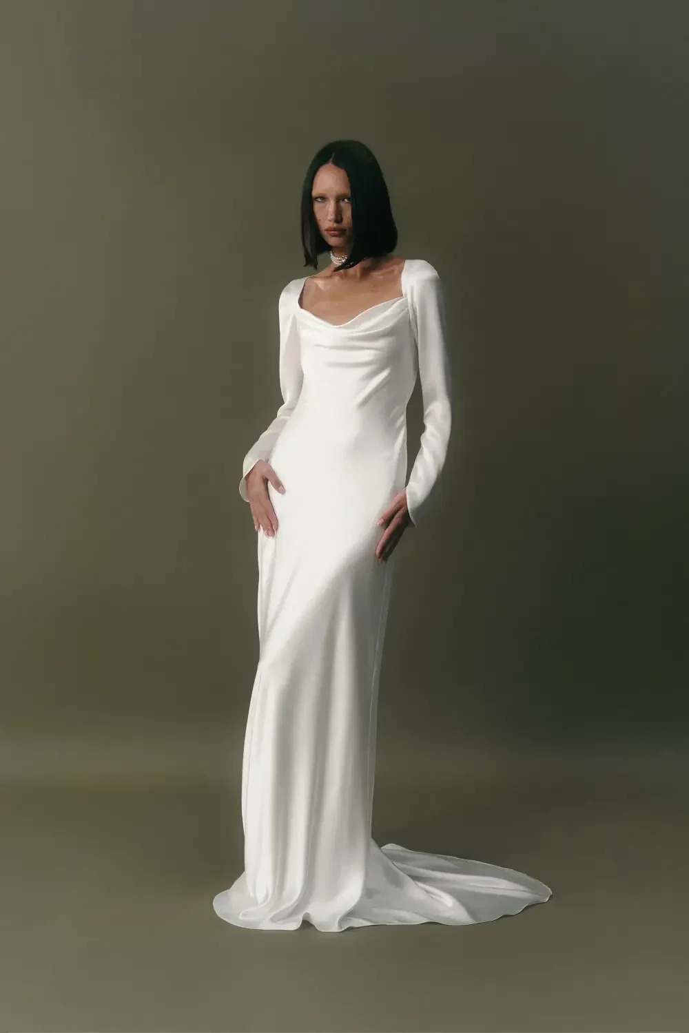 A model in a long, elegant white dress standing against a neutral background.