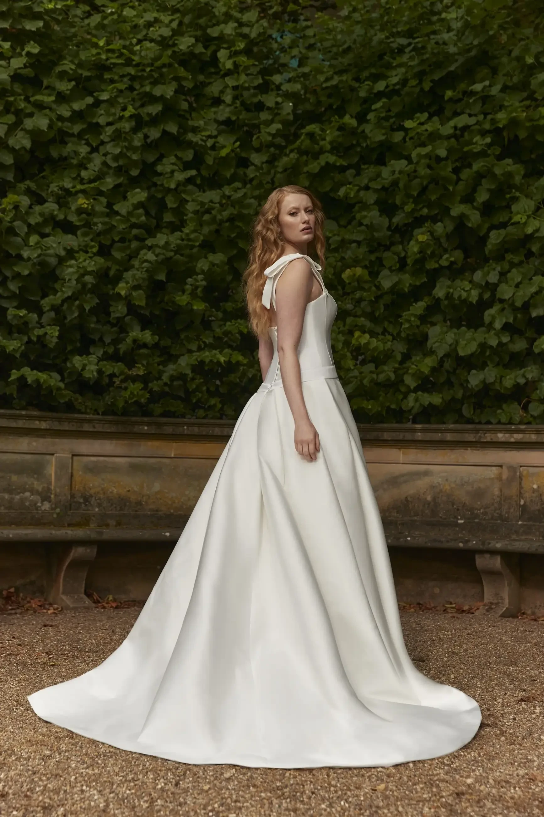 Model is wearing a strapless dropped waist gown with a micro jacquard corset and a bias-pleated full skirt.