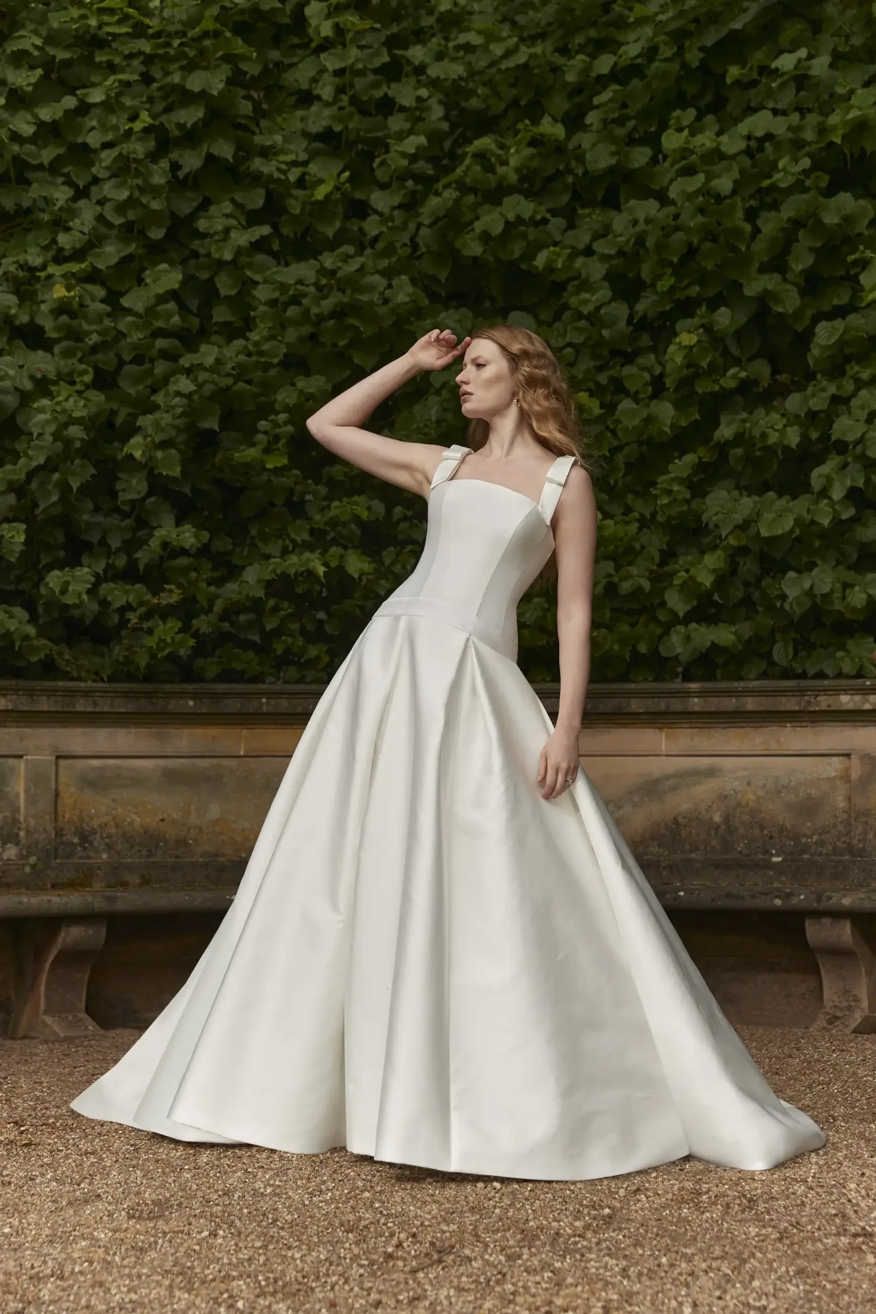Model is wearing a strapless dropped waist gown with a micro jacquard corset and a bias-pleated full skirt.