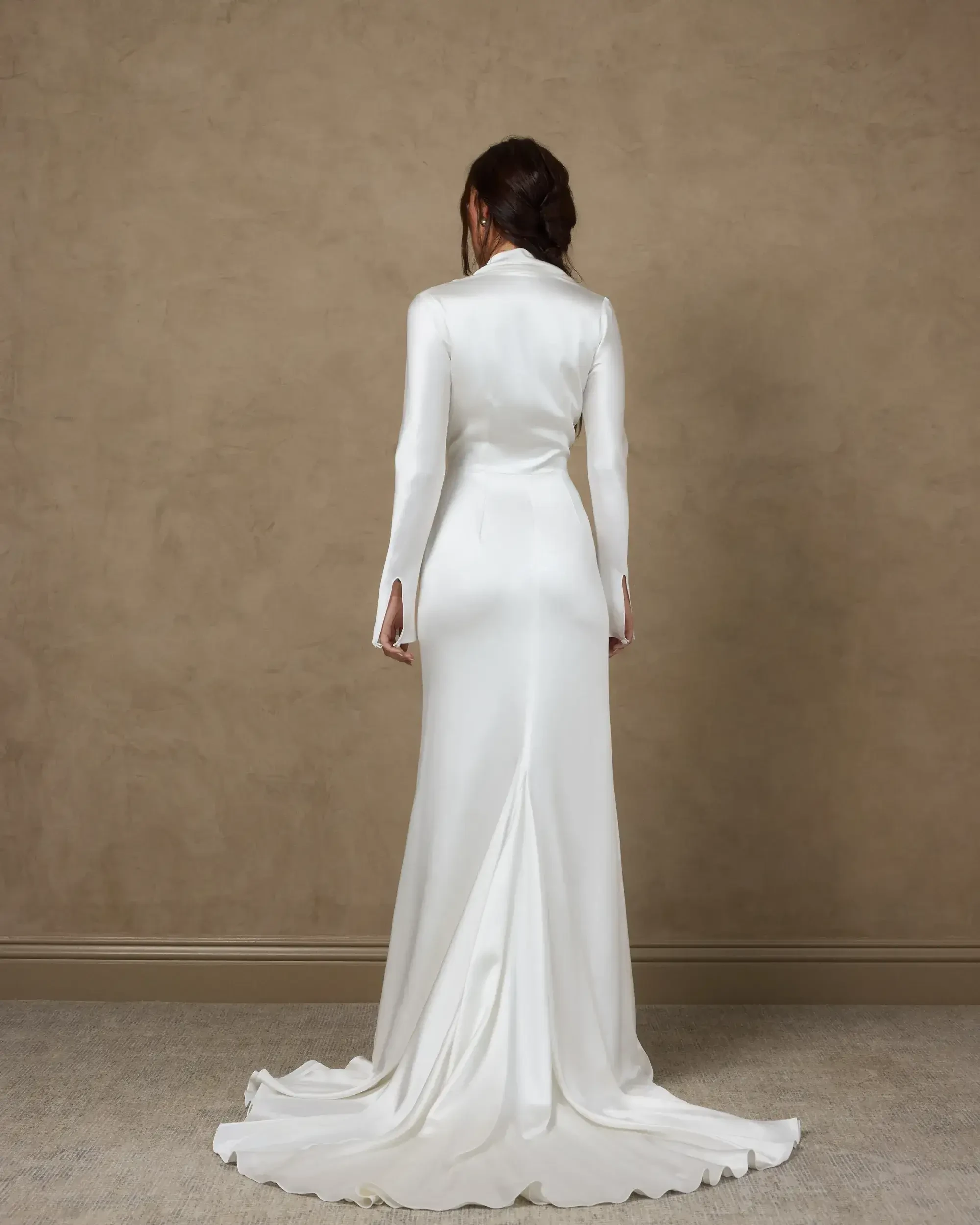 Model is wearing a bias-cut silk satin crepe gown with long sleeves, asymmetric neckline, leg slit, and side zipper with pearl buttons.