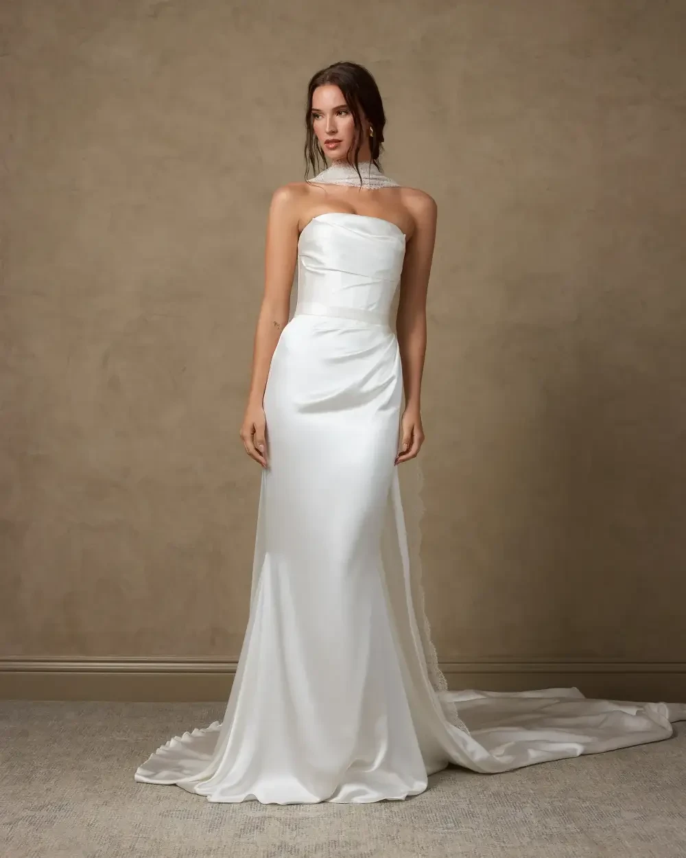 A model wearing a sleek, strapless white gown with a fitted silhouette and a train, posed against a neutral background.